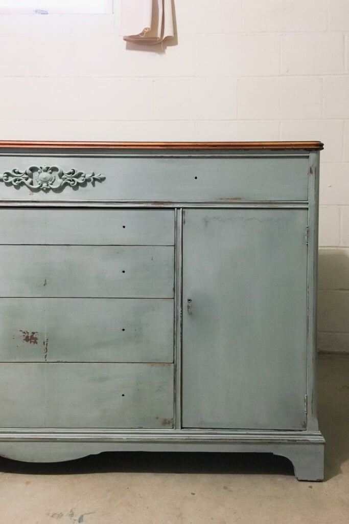 Distressed light green buffet with five drawers and a cabinet door, against a white wall.