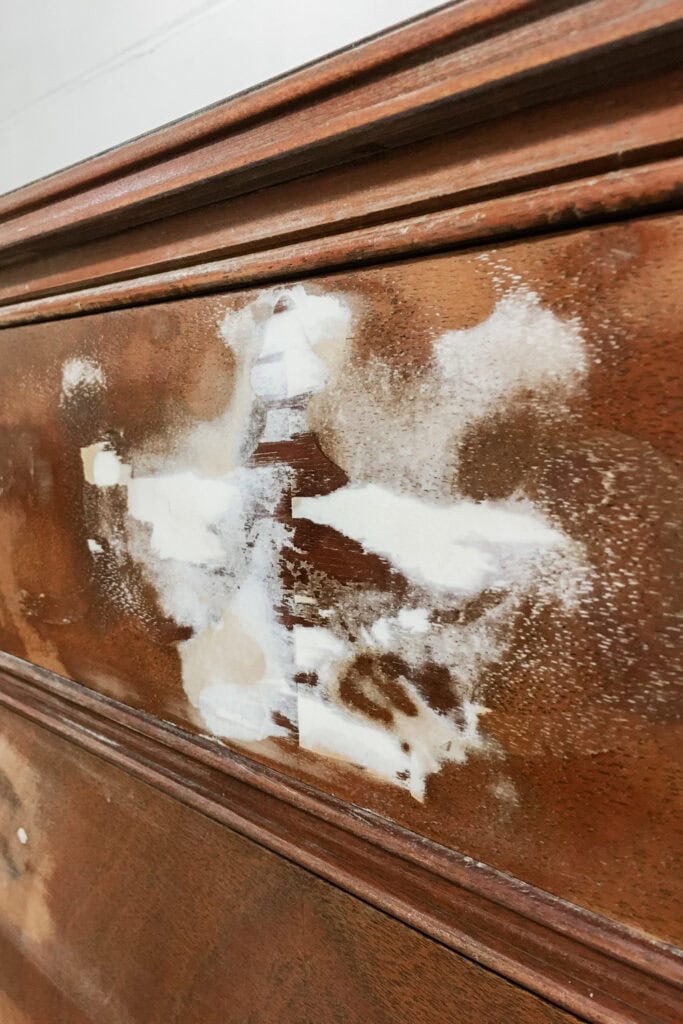 Close-up of a wooden surface with white filler patches applied over scratches and blemishes.