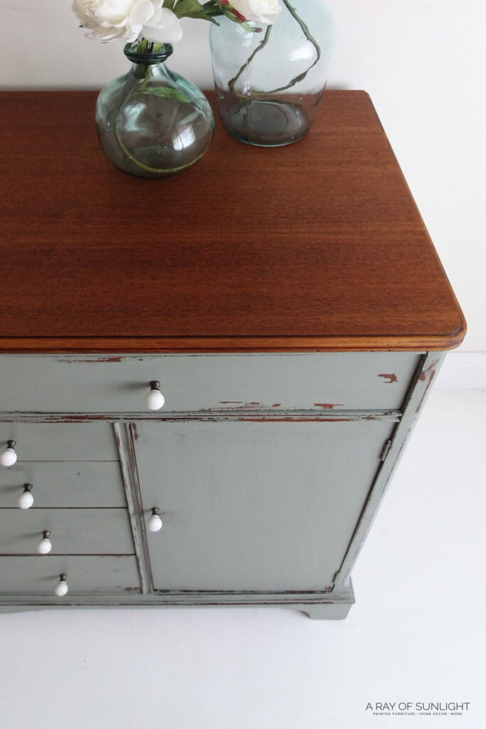 Distressed seafoam green sideboard with white knobs and wood top, decorated with glass vases and white flowers.