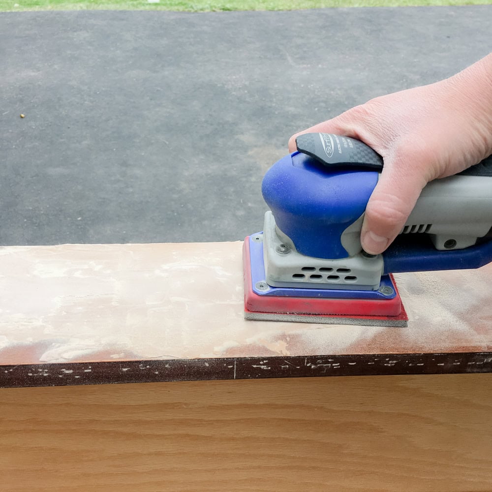 Hand using an electric sander on a wooden surface outdoors.