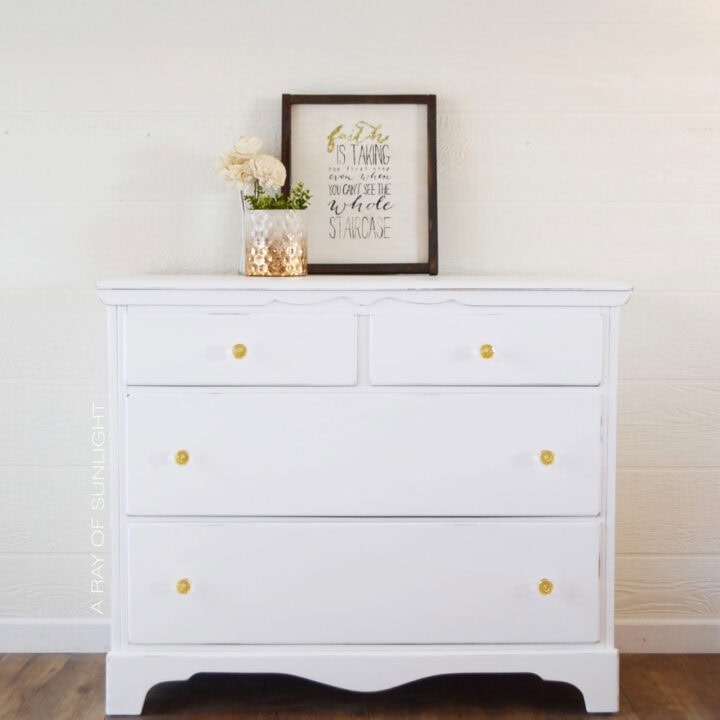 White dresser with gold knobs, with a framed quote and flowers on top