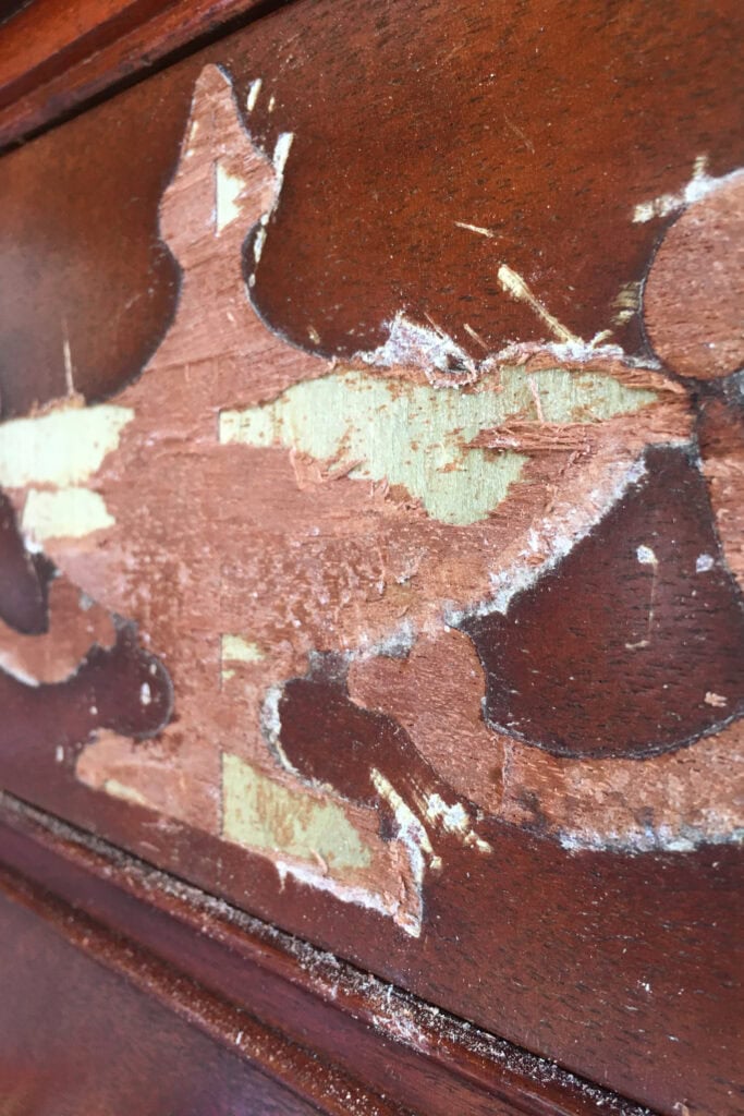 Close-up of scratched, partially removed wood veneer after removing emblem.