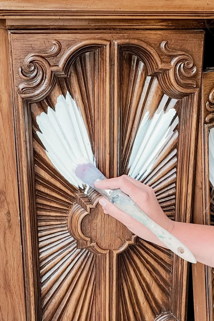 A hand brushing white strokes on an ornate laminate cabinet door