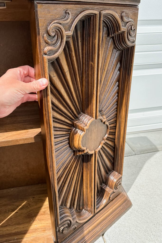 A hand holding a plastic cabinet door with ornate details.