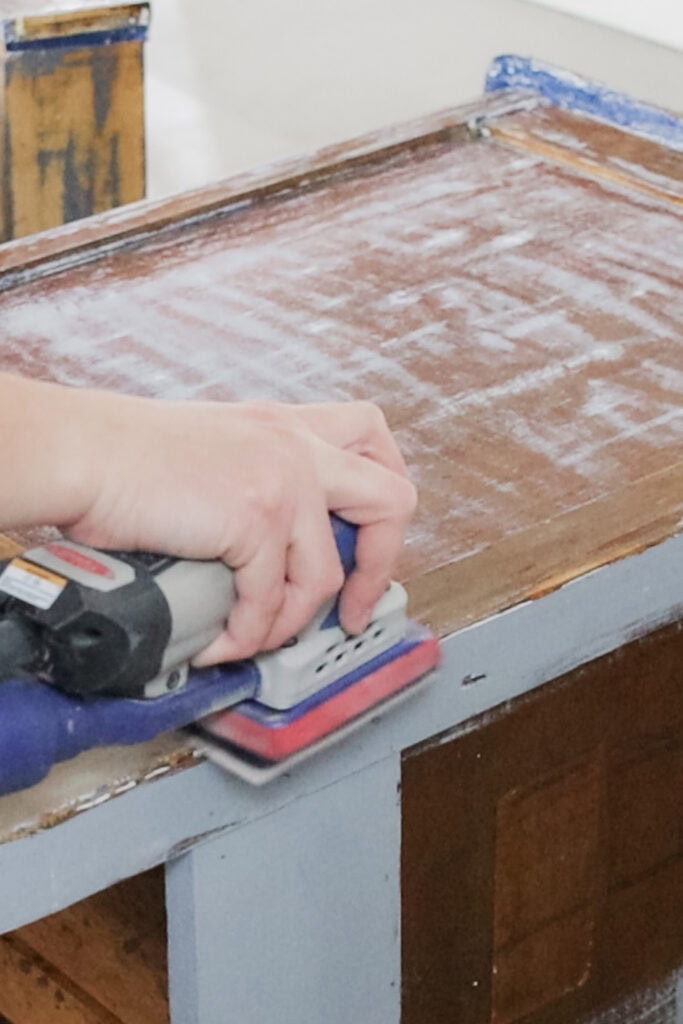 A person uses a sander to smooth the surface of a wooden top.