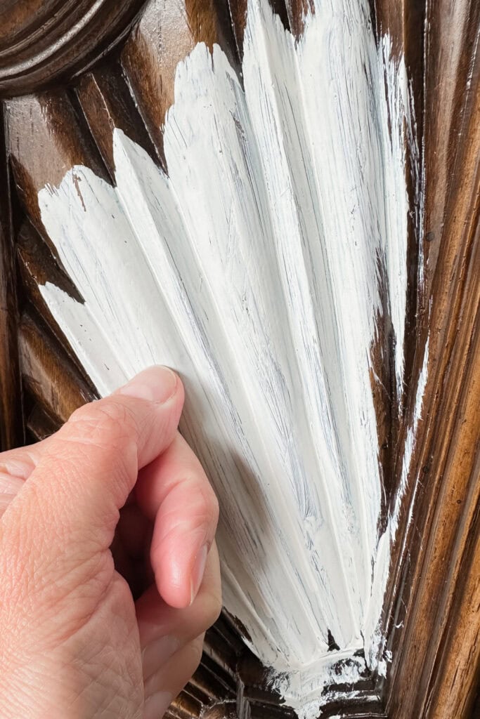 A hand scratching white paint on carved laminate wood looking surface.