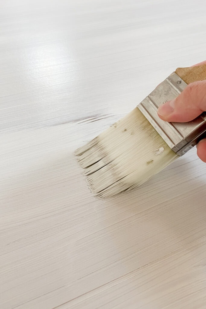 Applying white paint to a wooden surface using brush