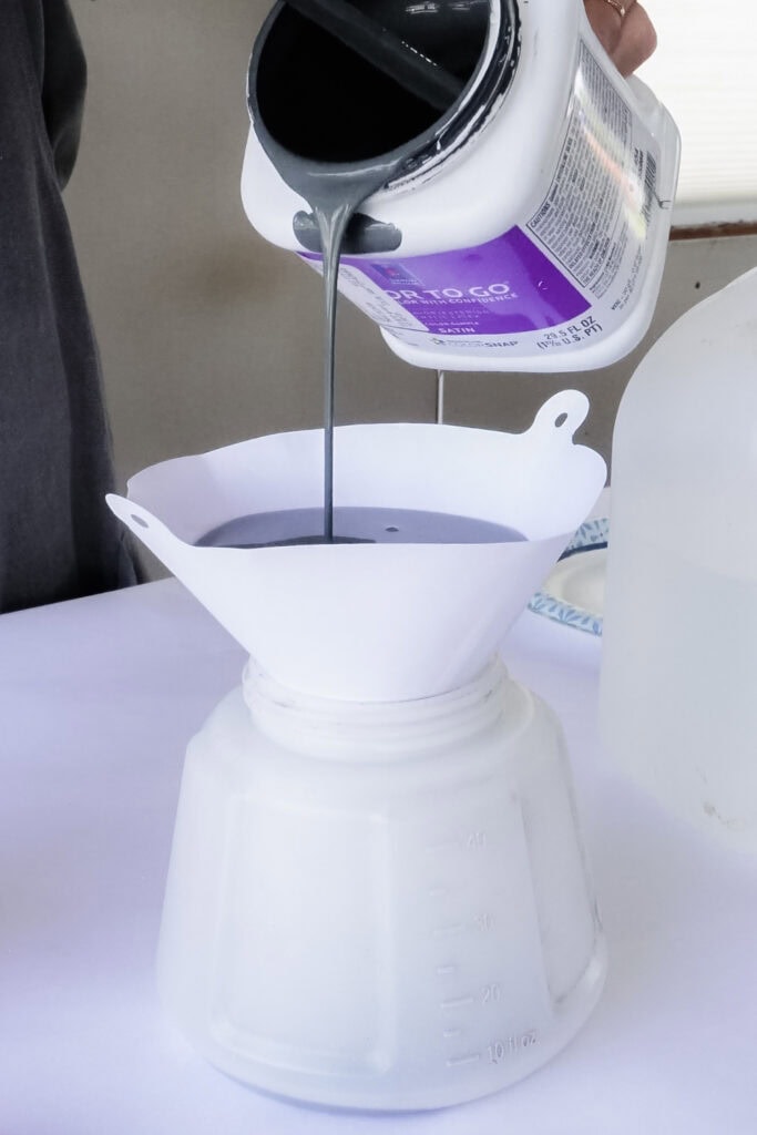 Paint being poured through a white paper filter into sprayer container