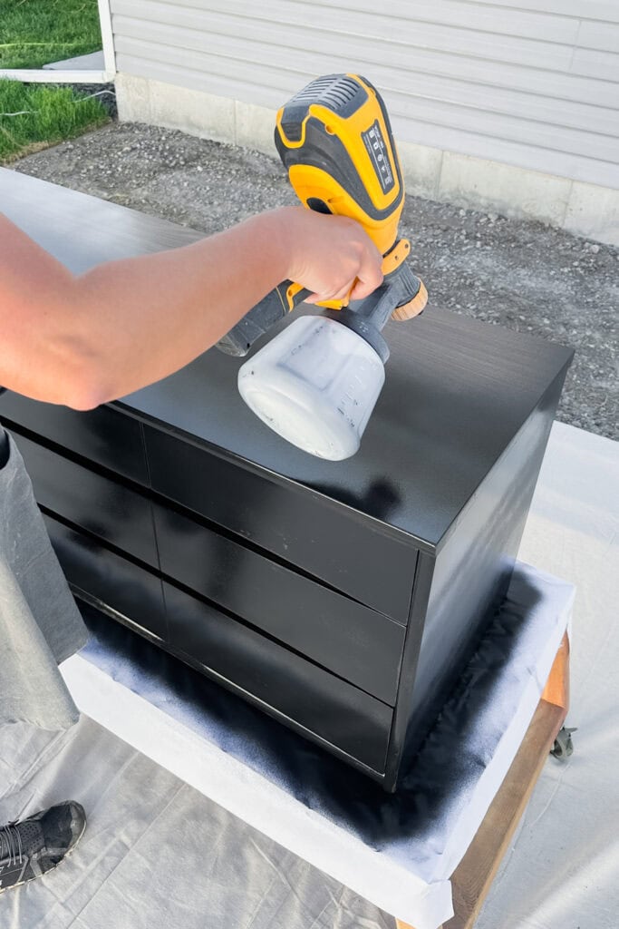 Spraying thin black coats of paint on dresser outdoors