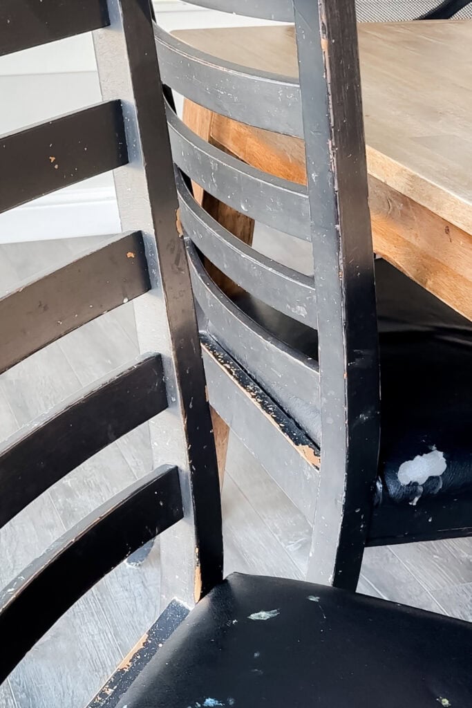 Two black wooden chairs with chipped paint and worn cushions