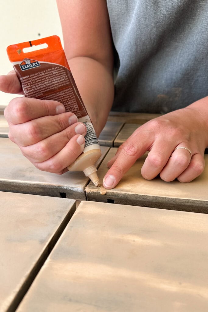 A person squeezes wood filler into scratches on wood furniture