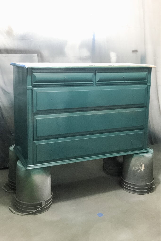 A teal dresser on top of upside-down buckets in a workshop.