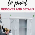 Using a paint sprayer to paint a cabinet with ornate grooves and details.