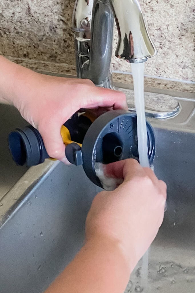 Hands cleaning a paint sprayer part under running water