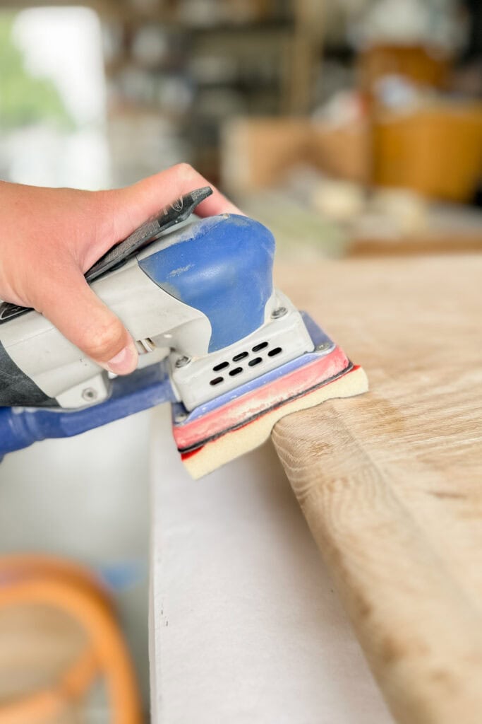 Using an electric sander to smooth the edge of a curved surface.