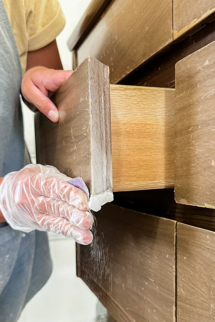A person sanding the edge of a wooden drawer