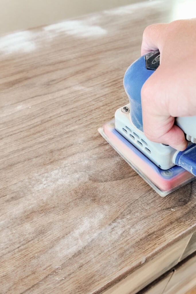 A hand using an electric sander to smooth a wooden surface