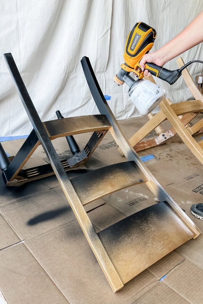 Using a paint sprayer to apply black finish on wooden chair