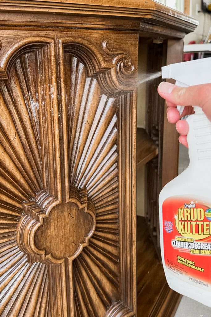 Hand spraying Krud Kutter cleaner onto ornate cabinet