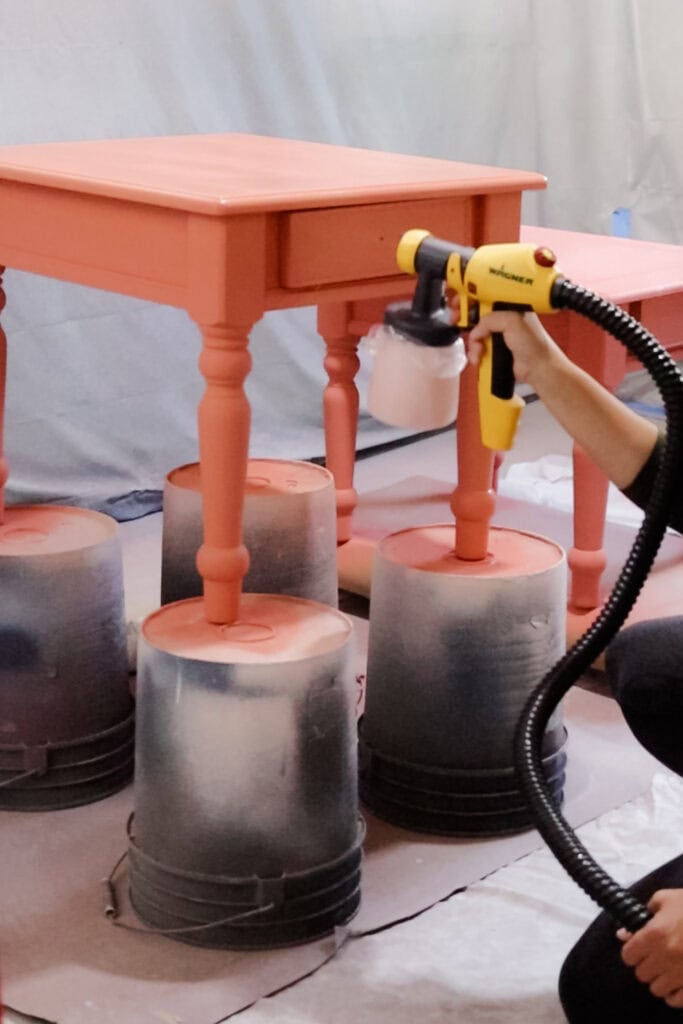 A person spray paints a small table placed on upside down buckets