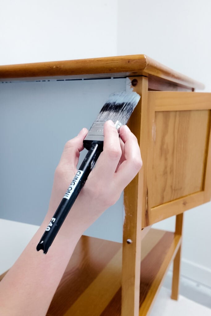 A hand painting a wooden cabinet blue with a brush