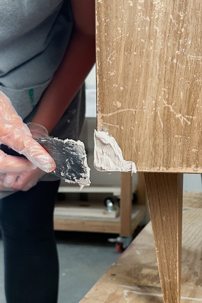 Person applying wood filler using a putty knife.