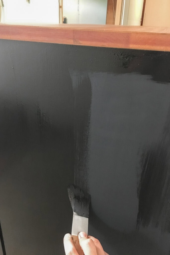 A hand using a brush to apply black paint on wooden surface