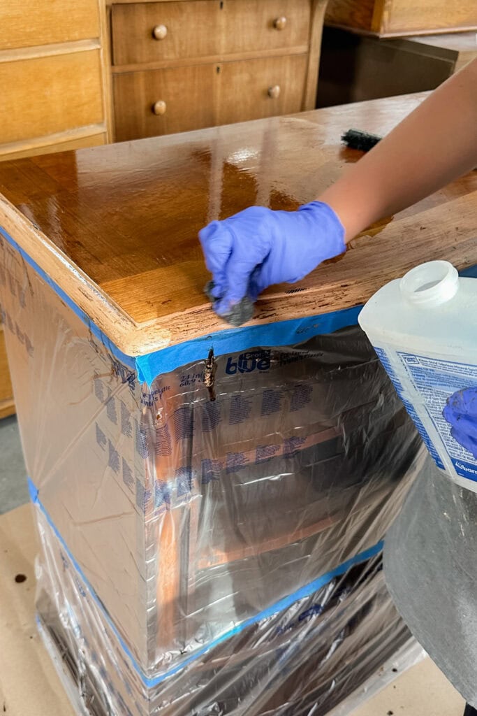 A person in gloves wipes wood surface clean with steel wool and mineral spirits