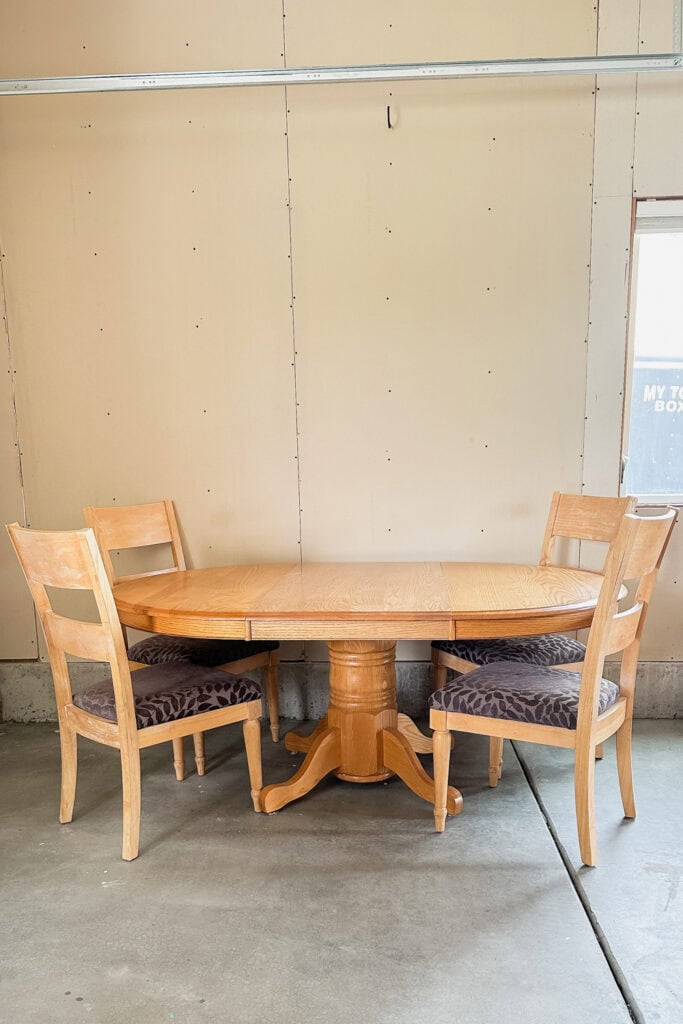A wooden oval table with four chairs, set in a garage