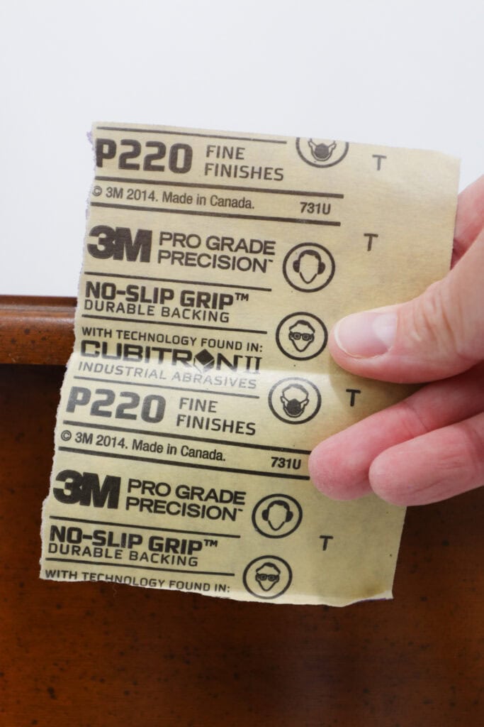 A hand holds 3M 220 grit sandpaper