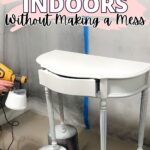 White table on paint cans being spray painted indoors; text reads “How to Paint Furniture Indoors Without Making a Mess.”.