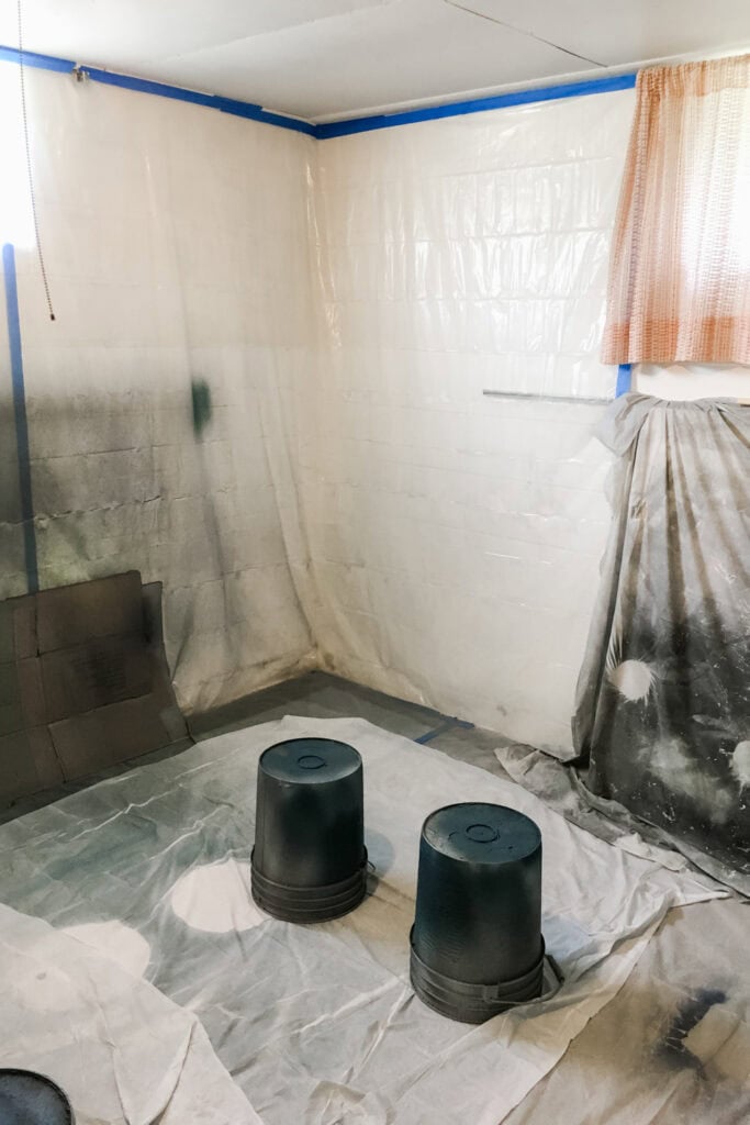 A room prepared for painting with coverings on walls and floor, and two buckets set upside down