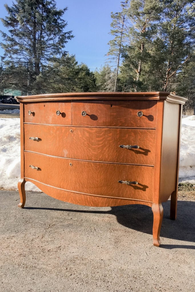 A vintage wooden dresser with curved legs stands outdoors
