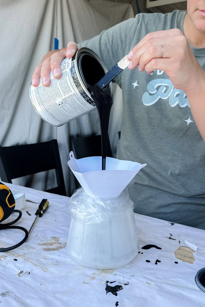 Person pouring black paint through a filter into a sprayer container