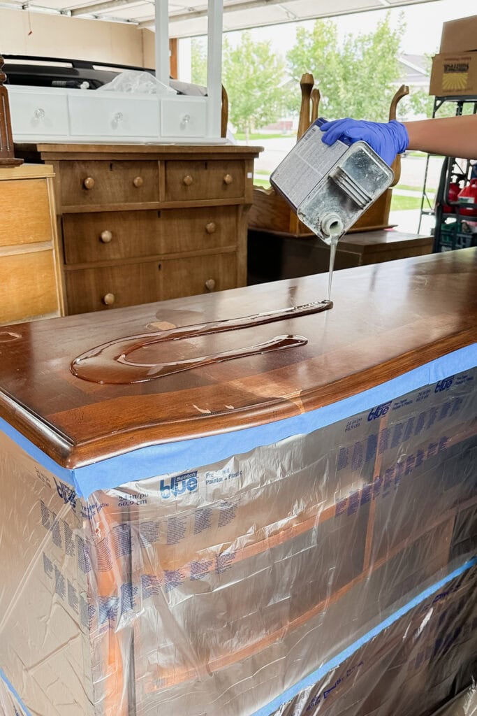 A person pours chemical stripper onto a wooden top