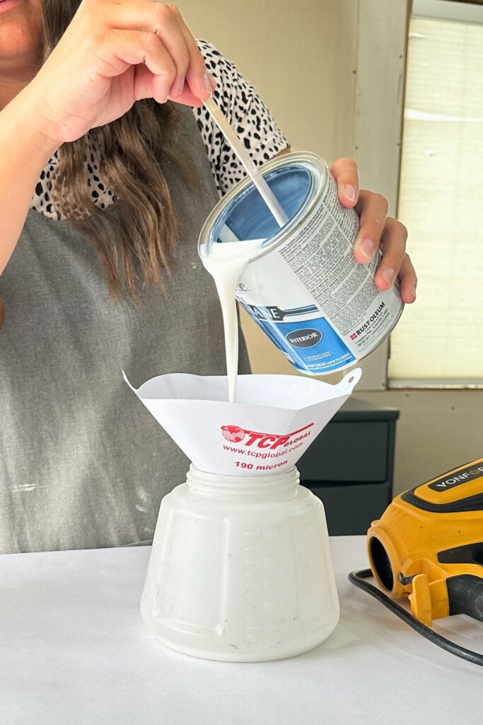 Person pouring waterbased poly from a can through a paper filter into a sprayer container.
