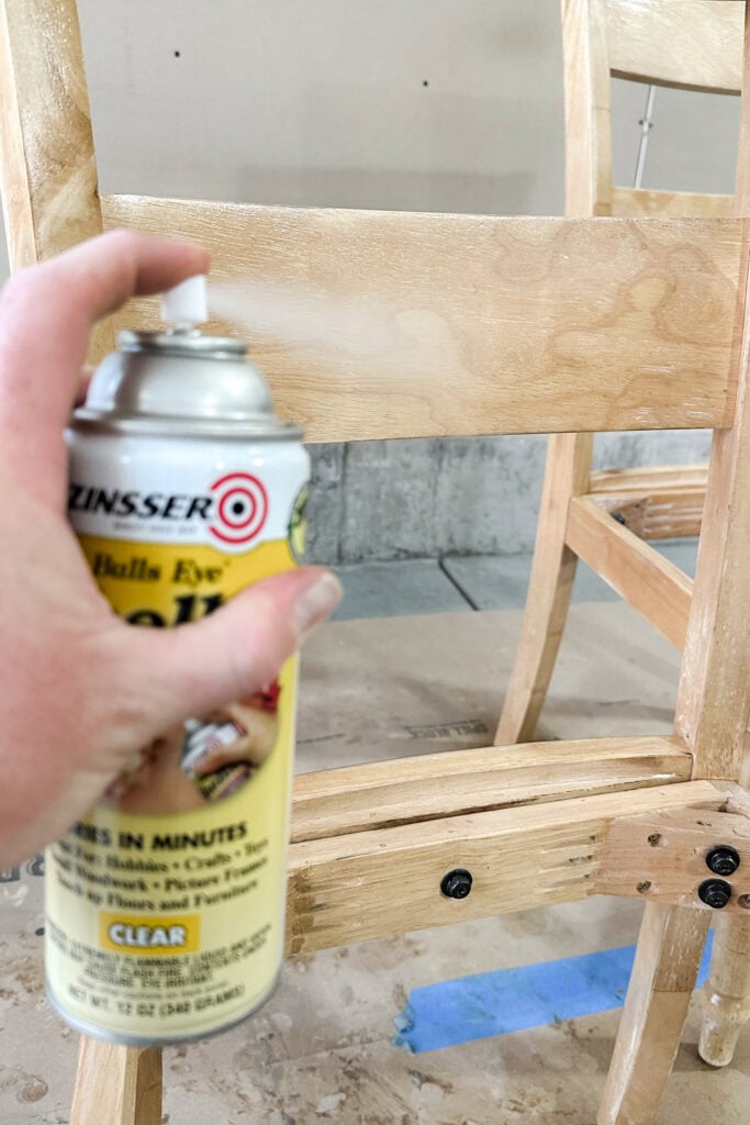 A hand sprays clear shellac onto a chair frame