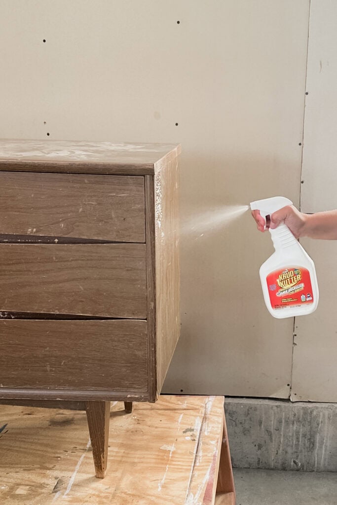 A hand sprays Krud Kutter cleaner onto a wooden dresser