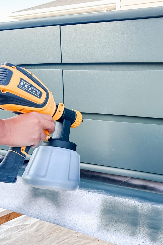 A person uses a paint sprayer to apply green paint