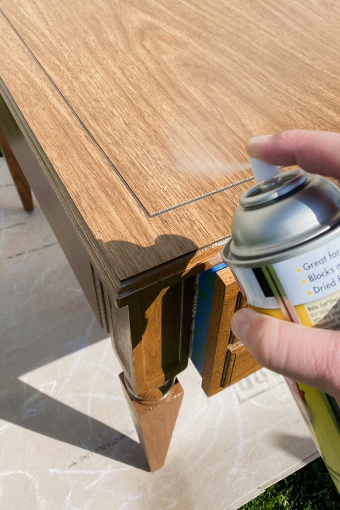 Hand spraying clear shellac onto a wooden table