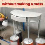 Person spray painting a small white table indoors