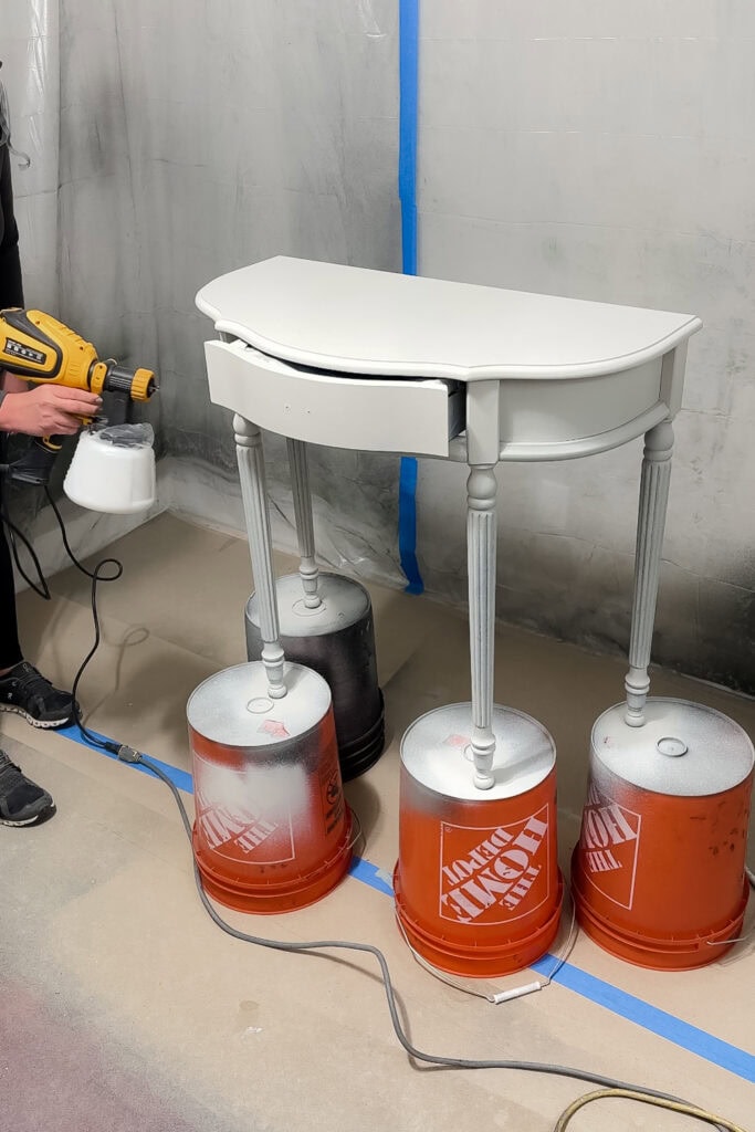A person spray painting a table on top of four buckets