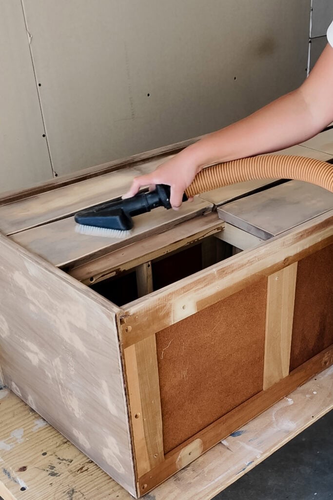 A person uses a vacuum to clean dust on wooden furniture