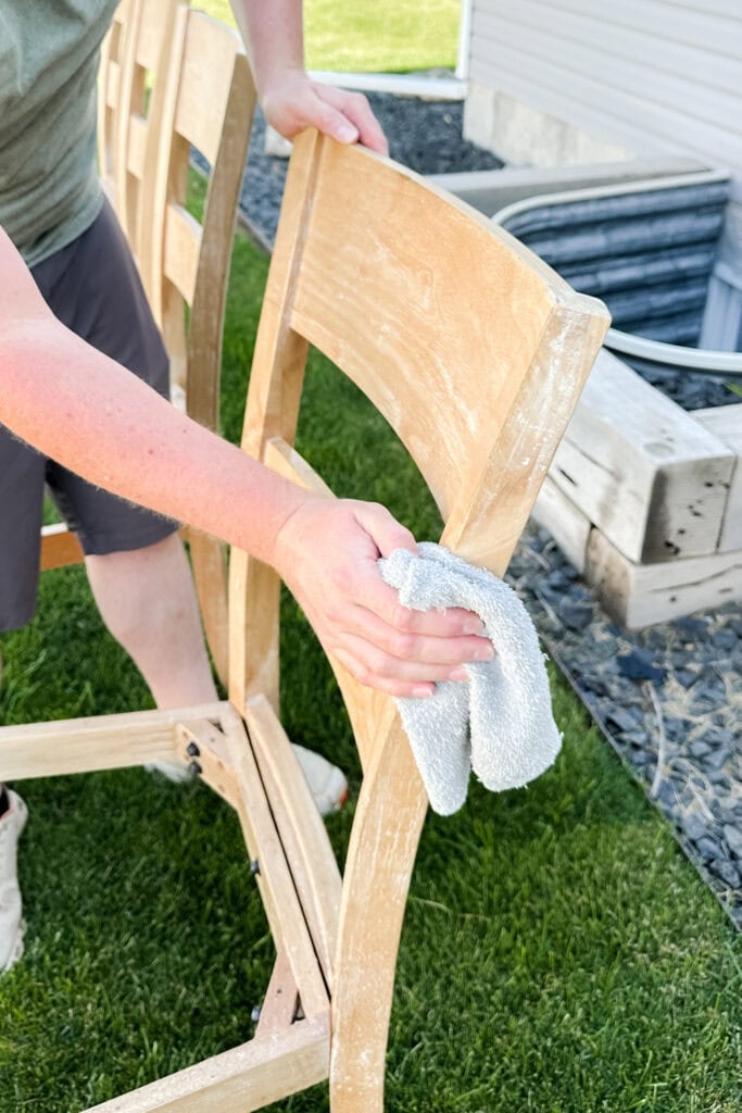 Person cleaning a wooden chair outdoors with a gray rag