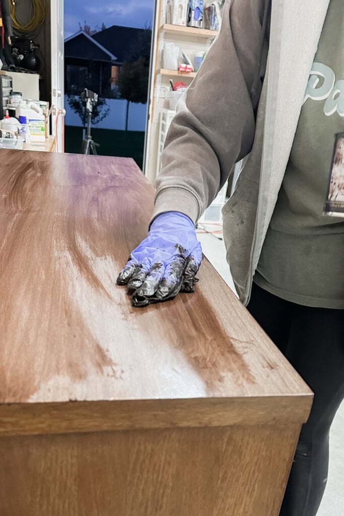 Person wearing a glove staining a wooden surface in a garage
