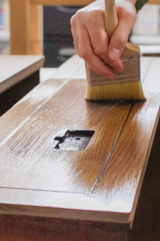 A hand uses a brush to apply topcoat to a wooden drawer