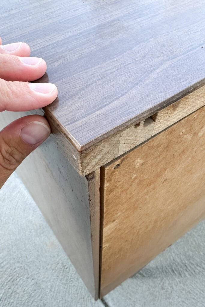 A hand touching a laminate and wooden dresser.