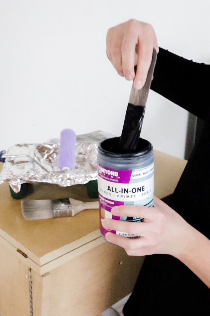 A person dipping a stirrer into an open paint container