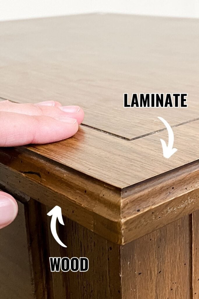 A hand touches the edge of a table showing laminate and wood sections