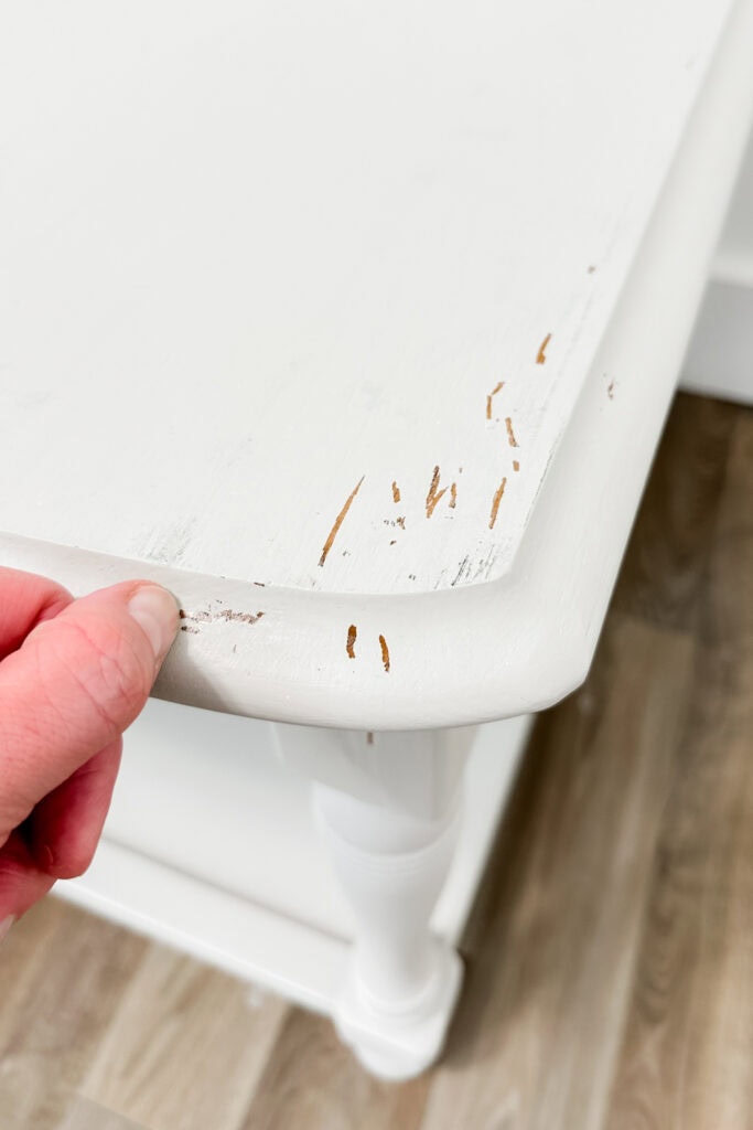 A hand scratching white paint on furniture